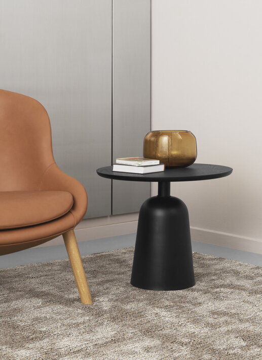 Široká dizajnová váza z hnedého skla na čiernom príručnom stolíku pri hnedom kresle