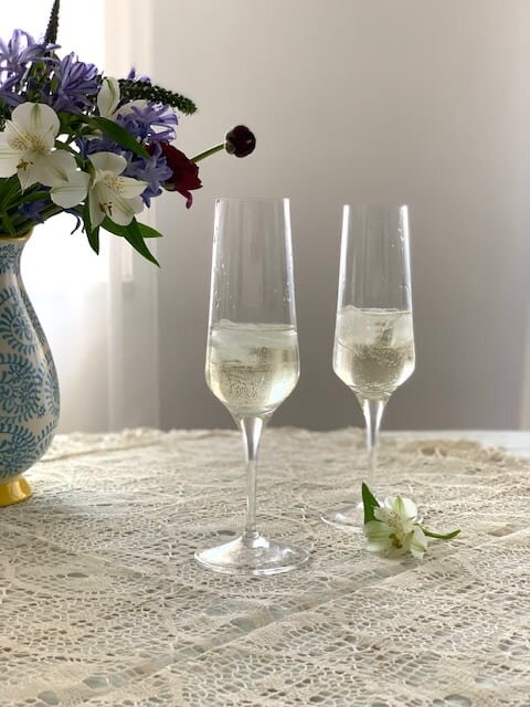Úzke minimalistické krištáľové poháre so šampanským a ľadom pri váze s kvetmi