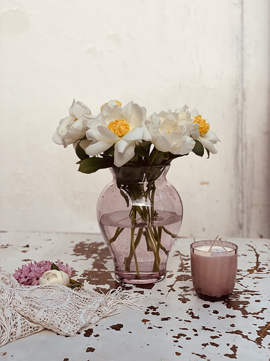 Dizajnová váza z fialového krištáľu s bielymi kvetmi pri sviečke