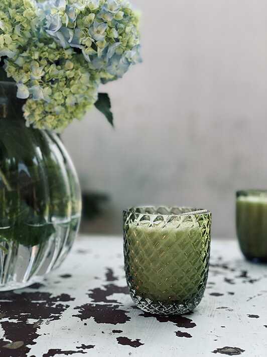 Malá vonná sviečka v zelenom krištáľovom pohári s prešívaným vzorom pri vázičke