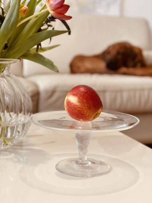 Červené jablko na krištáľovom tortovom podnose na stole v obývačke