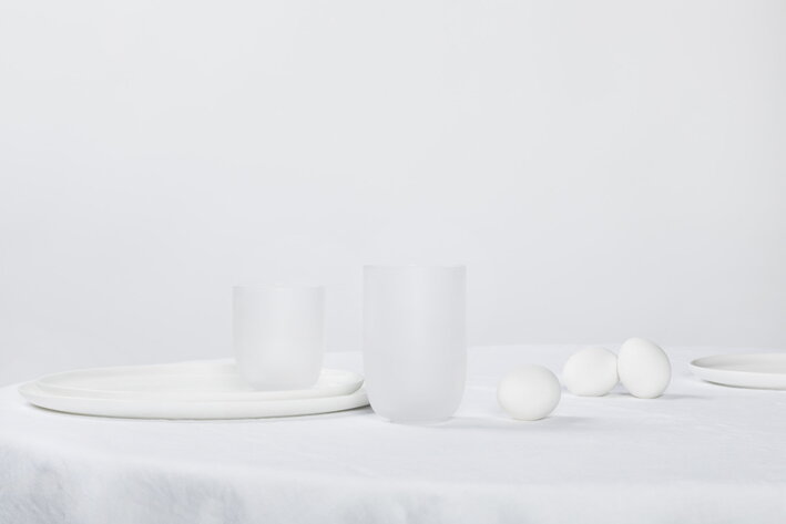 Okrúhly biely podnos na stole s matnými pohármi na vodu pri varených vajíčkach