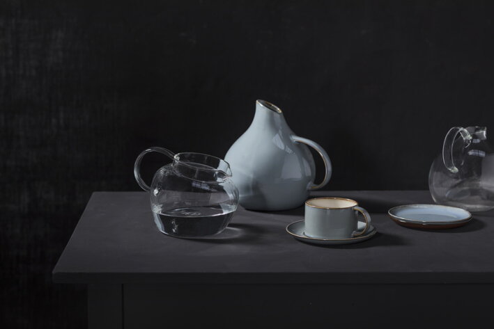 Sivomodrá keramická podšálka so šálkou na kávu pri dizajnových sklenených a keramických džbánoch
