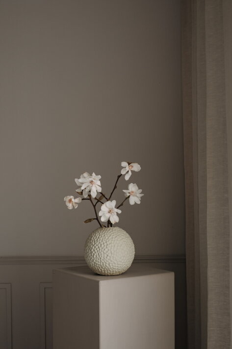 Malá guľatá váza z krémovej keramiky s kyticou kvetov na stole