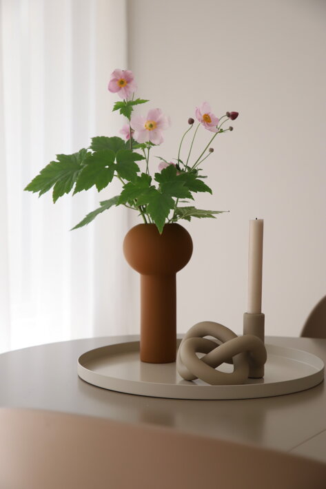 Pieskový okrúhly podnos z kovu na jedálenskom stole s vázou a svietnikom
