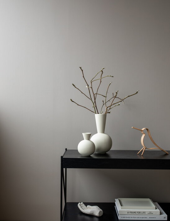 Nízka dizajnová váza z krémovej keramiky s halúzkami na stole