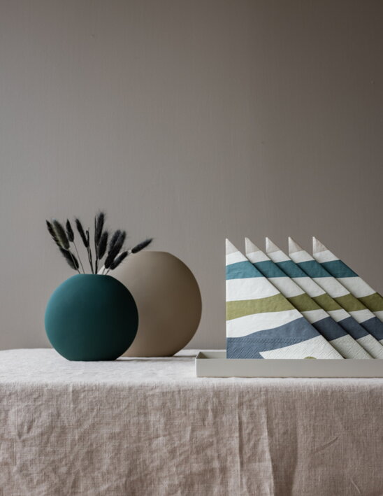 Dizajnové servítky s abstraktnými čiarami v lesných farbách zložené na stole s vázou
