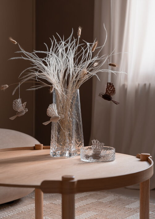 Dekoračný papierový vtáčik na vetvičke v sklenenej váze v obývačke