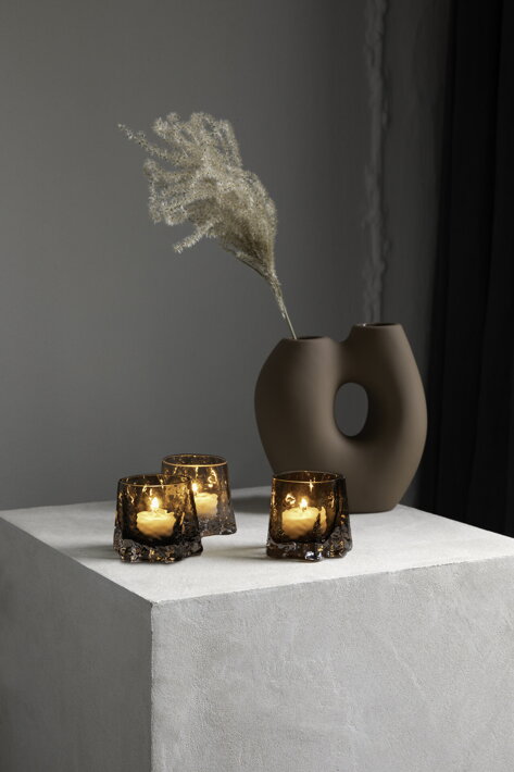 Tri hnedé sklenené svietniky s čajovými sviečkami pri dizajnovej váze