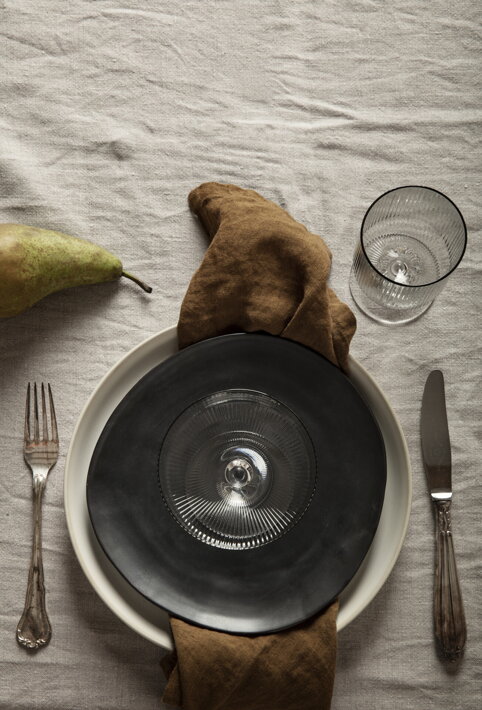 Slávnostné prestieranie - veľký krémový tanier, malý čierny tanier a vrúbkovaný sklenený pohár