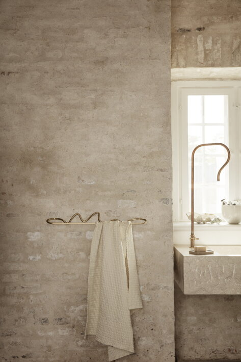 Nepravidelný mosadzný vešiak s béžovým uterákom pri mramorovom umývadle v kúpeľni