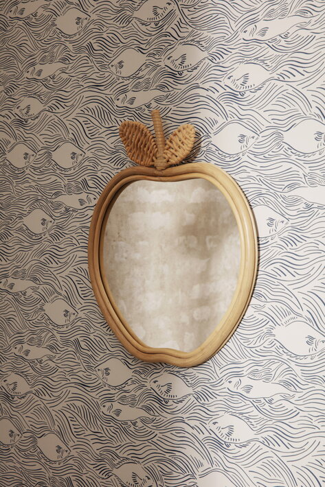 Detské zrkadlo v tvare jablka s prírodným ratanovým rámom na stene s modrou tapetou