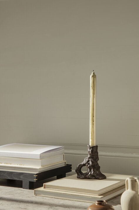 Vysoká biela sviečka so zeleným kvapkaným efektom v dizajnovom hnedom svietniku