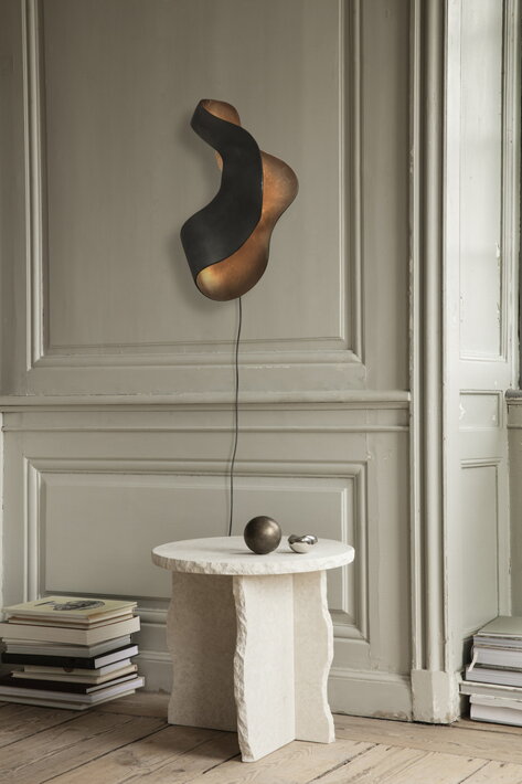 Dizajnová nepravidelná lampa z čierneho kovu na stene v obývačke nad mramorovým stolíkom