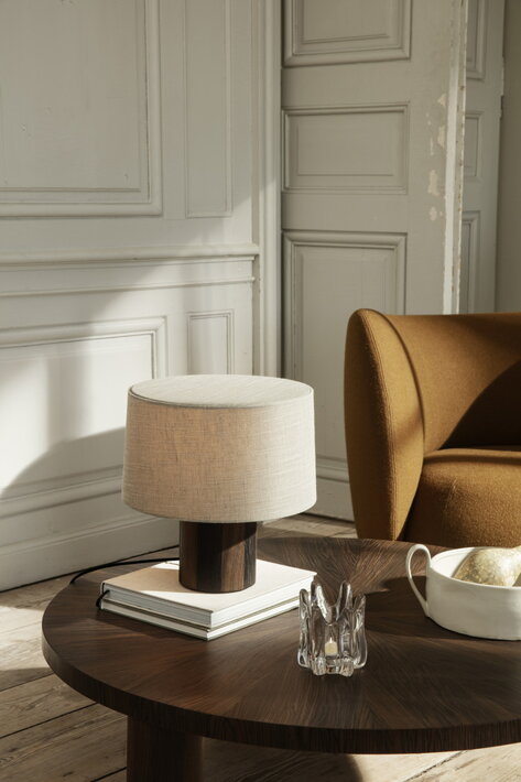 Elegantná stolová lampa s drevenou základňou a bavlneným tienidlom na príručnom stolíku v obývačke