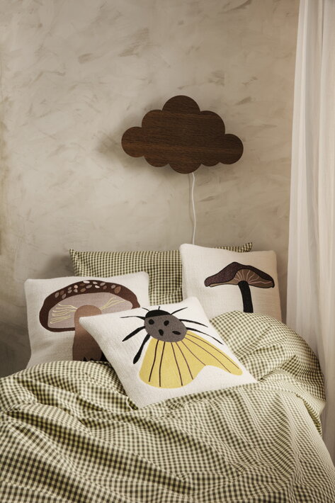 Vlnený vankúš s výšivkou nočného motýľa na posteli pod drevenou lampou