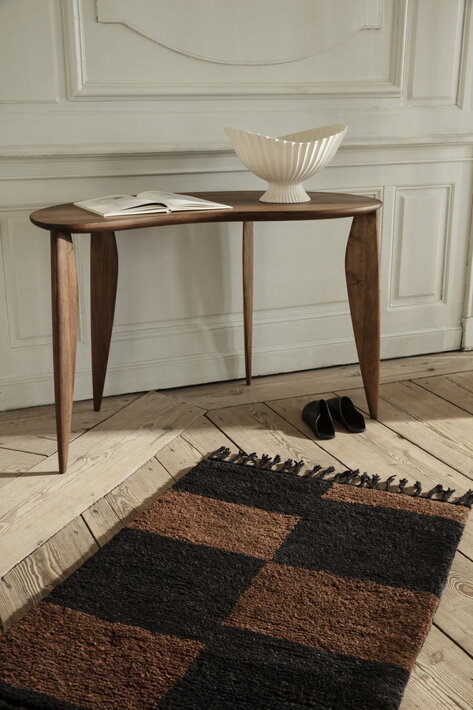 Menší tkaný koberec s ozdobnými strapcami pri dizajnovom stole v spálni