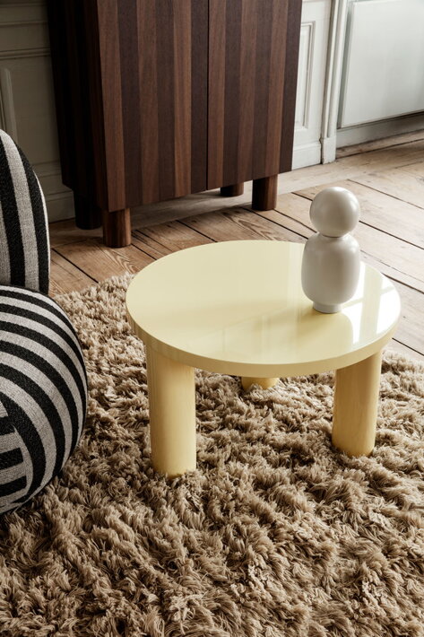 Lakovaný žltý okrúhly stolík s troma nohami v obývačke