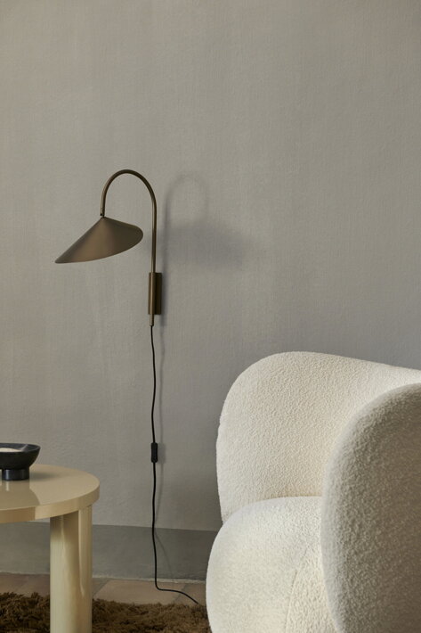 Minimalistická bronzová lampa na stene v obývačke pri dizajnovom kresle
