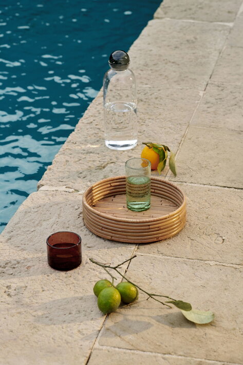 Okrúhly ratanový podnos s osviežujúcimi nápojmi pri vonkajšom bazéne