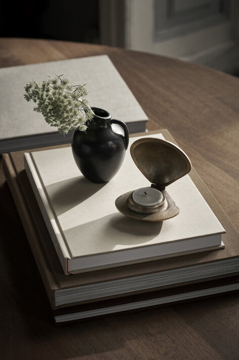 Mosadzný svietnik na čajovú sviečku v tvare mušle na stole v obývačke