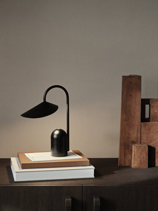 Prenosná lampa v čiernej farbe na knihách umiestnených na komode