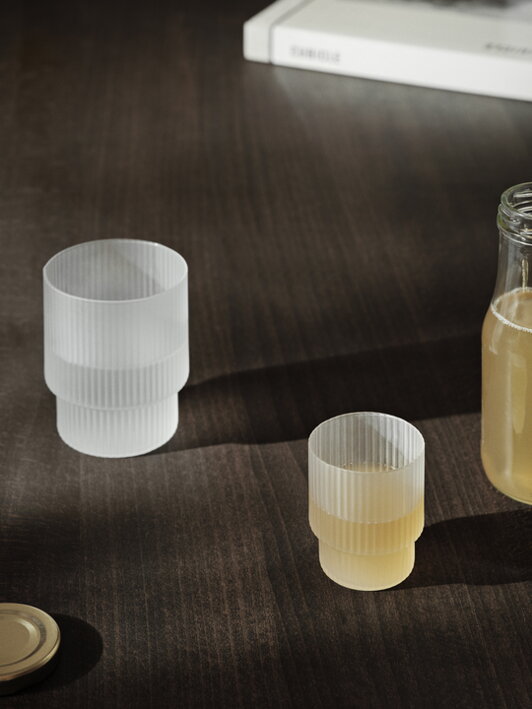 Dva matné poháre rôznych geometrických tvarov na stole s naliatými nápojmi