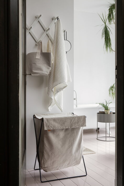 Plátený kôš na bielizeň na kovovej konštrukcii v bielej minimalistickej kúpeľni