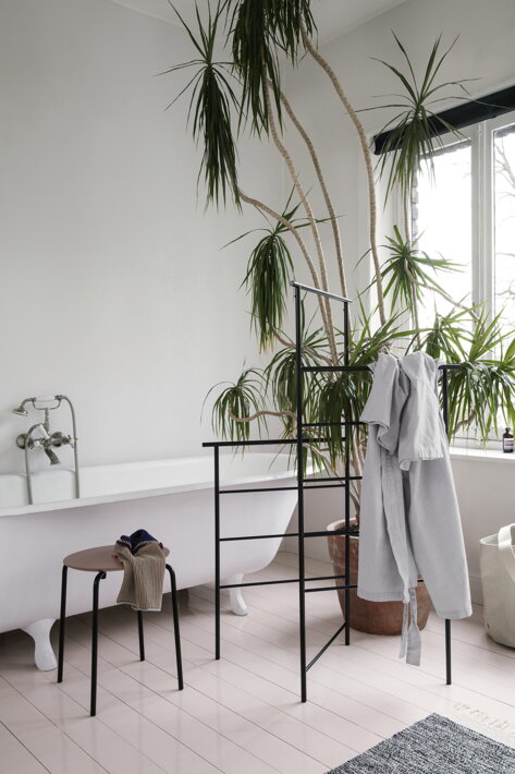 Čierna kovová konštrukcia na zavesenie oblečenia a uterákov v kúpeľni pri izbovej rastline