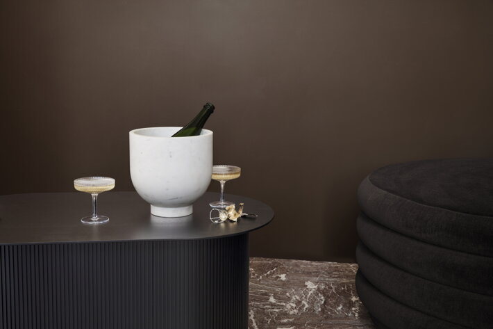 Biela mramorová misa na fľašu šampanského s vrúbkovanými slávnostnými pohármi na hnedom stole