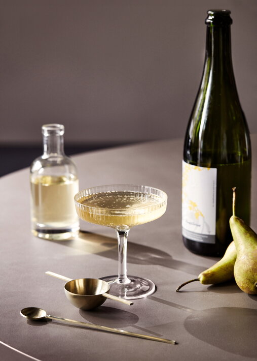 Široký vrúbkovaný pohár so šampanským na stole s hruškami a mosadznou lyžičkou