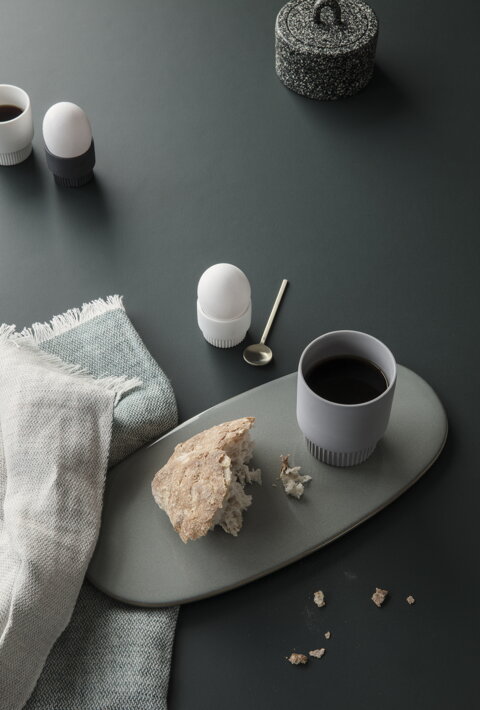 Malá mosadzná lyžička na vajíčko pri tanieri s kávou a chlebom