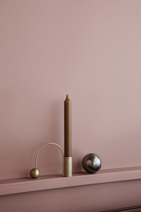 Mosadzný minimalistický svietnik so žltou vysokou sviečkou pri ružovej stene
