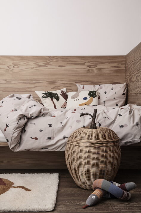 Detský vankúš s veselou výšivkou na posteli pri ratanovom koši v tvare jablka