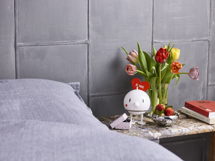 Veľká biela figúrka Hoptimista Love na nočnom stolíku s kvetmi a jahodami ako valentínsky darček