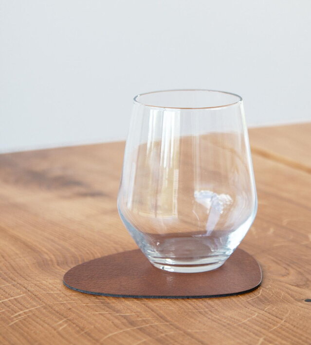 Podložka z recyklovanej kože vo farbe koňaku pod skleneným pohárom na drevenom stole
