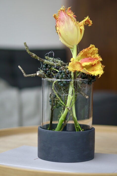 Čierna betónová váza so sklenenou vložkou s tulipánom a vetvičkami