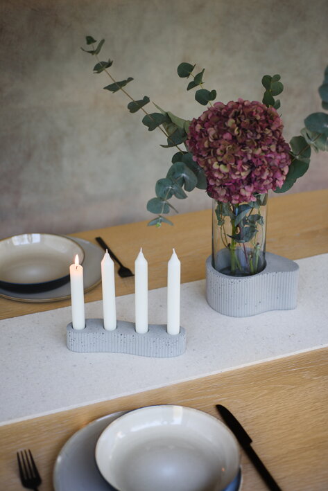 Sivý nízky svietnik na 4 sviečky z betónu na jedálenskom stole pri betónovej váze