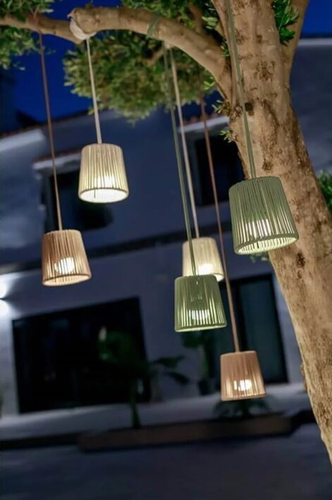 Viacero rozsvietených mini závesných lámp na strome vo večernej atmosfére