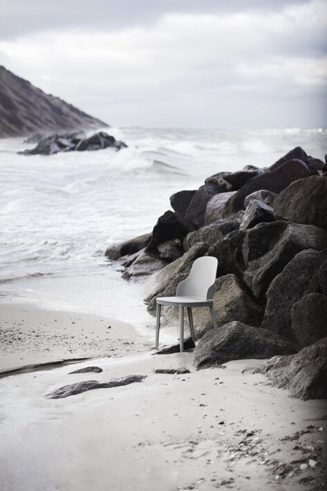 Opustená sivá plastová stolička na pláži pri skalách a mori
