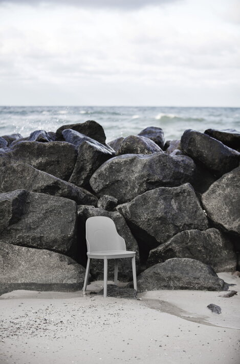 Opustená stolička na pláži pri skalách, za ktorými je more