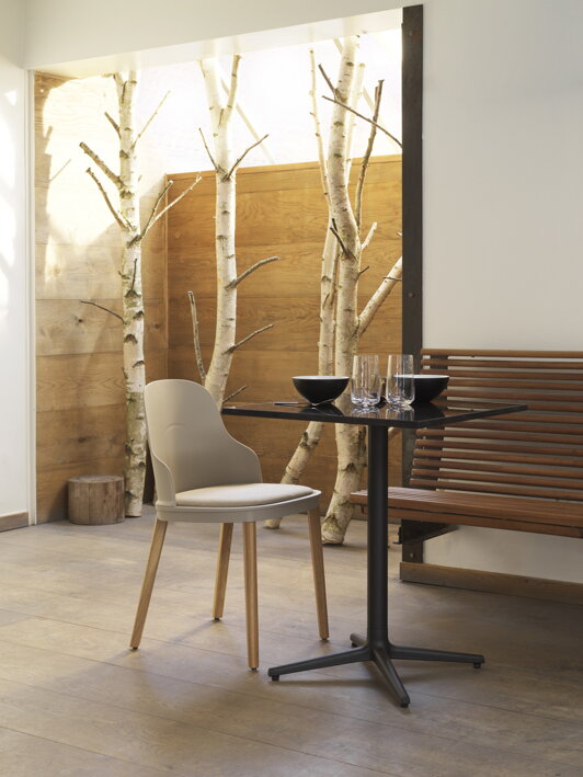 Stolička v teplej sivej farbe s dubovými nohami pri stolíku s pohármi a miskami
