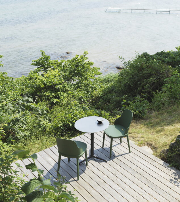 Tmavozelené dizajnové stoličky pri stolíku na teraze so zeleňou pri vode
