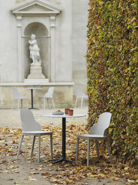 Okrúhly kaviarenský stôl s dvoma stoličkami v záhrade vedľa živého plotu v jesennej atmosfére