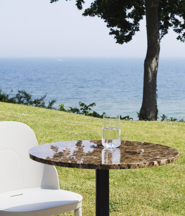 Hnedý mramorový okrúhly stôl s bielou stoličkou neďaleko morského pobrežia v pozadí so zeleňou a morom