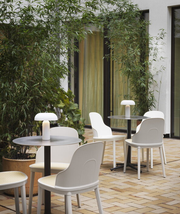 Dva malé okrúhlae kaviarenské stoly s prisunutými bielymi stoličkami na terase s rastlinnou dekoráciou