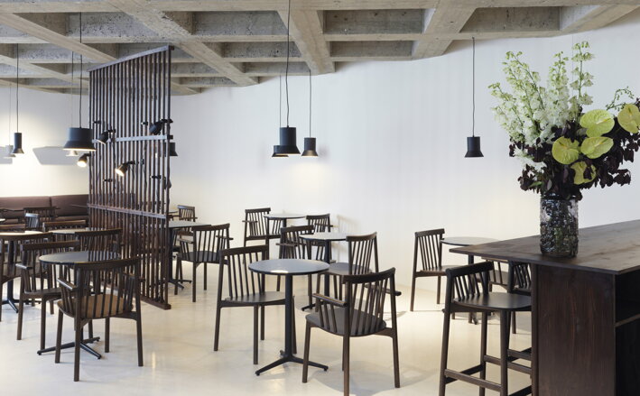 Niekoľko malých čiernych kaviarenských stolov so stoličkami v priestoroch kaviarne alebo reštaurácie
