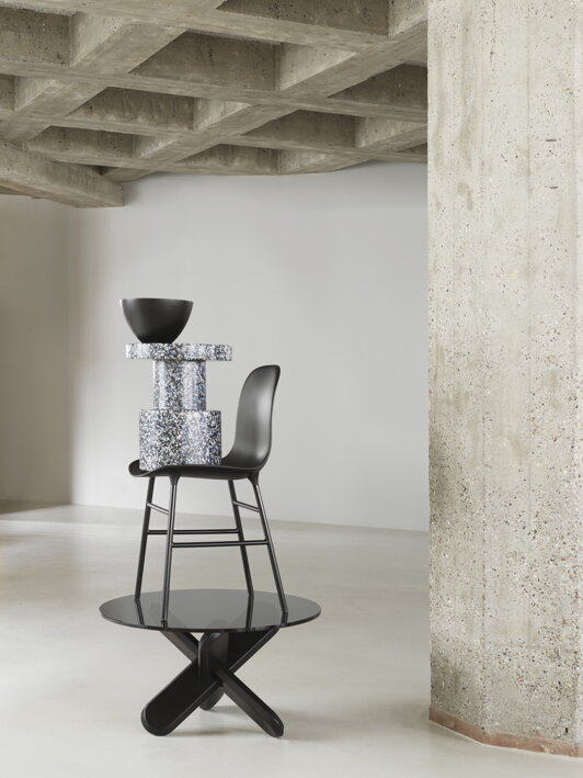 Nonferenčnom stolíku v miestnosti s betónovým stropom položená čierna stolička, príručný stolík a miska