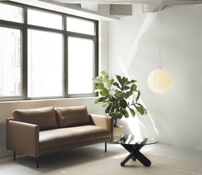 Konferenčný stolík v presvetlenej obývačke pred hnedou pohovkou a izbovou rastlinou