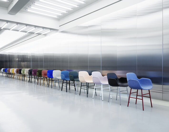 Dlhý rad jedálenských stoličiek s podrúčkami rôznych farieb pri chrómovej stene vo veľkej svetlej miestnosti